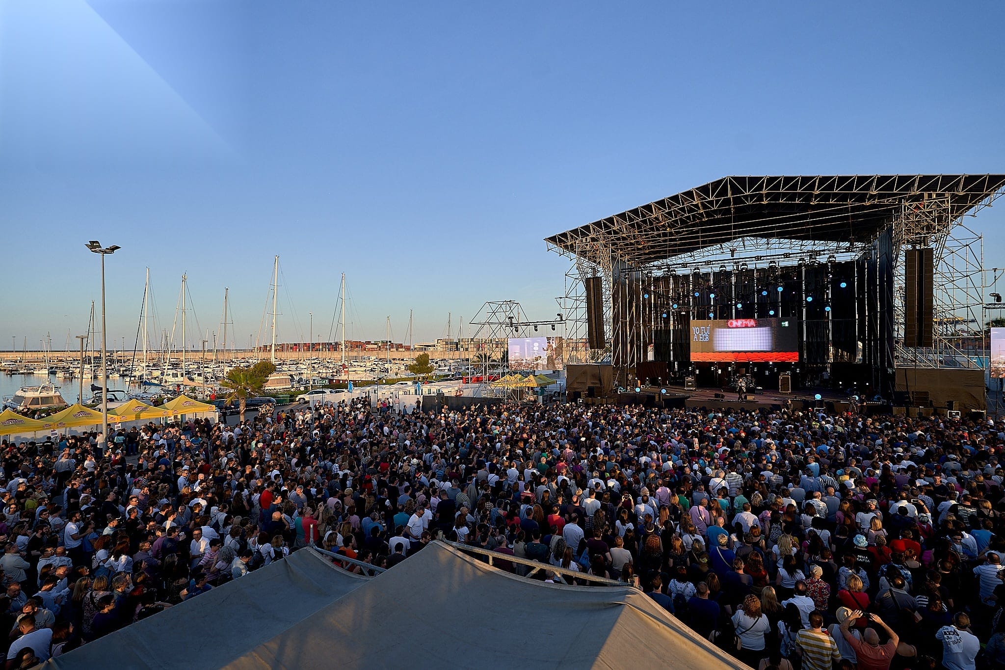 Escenario al aire libre junto al puerto deportivo, lleno de público