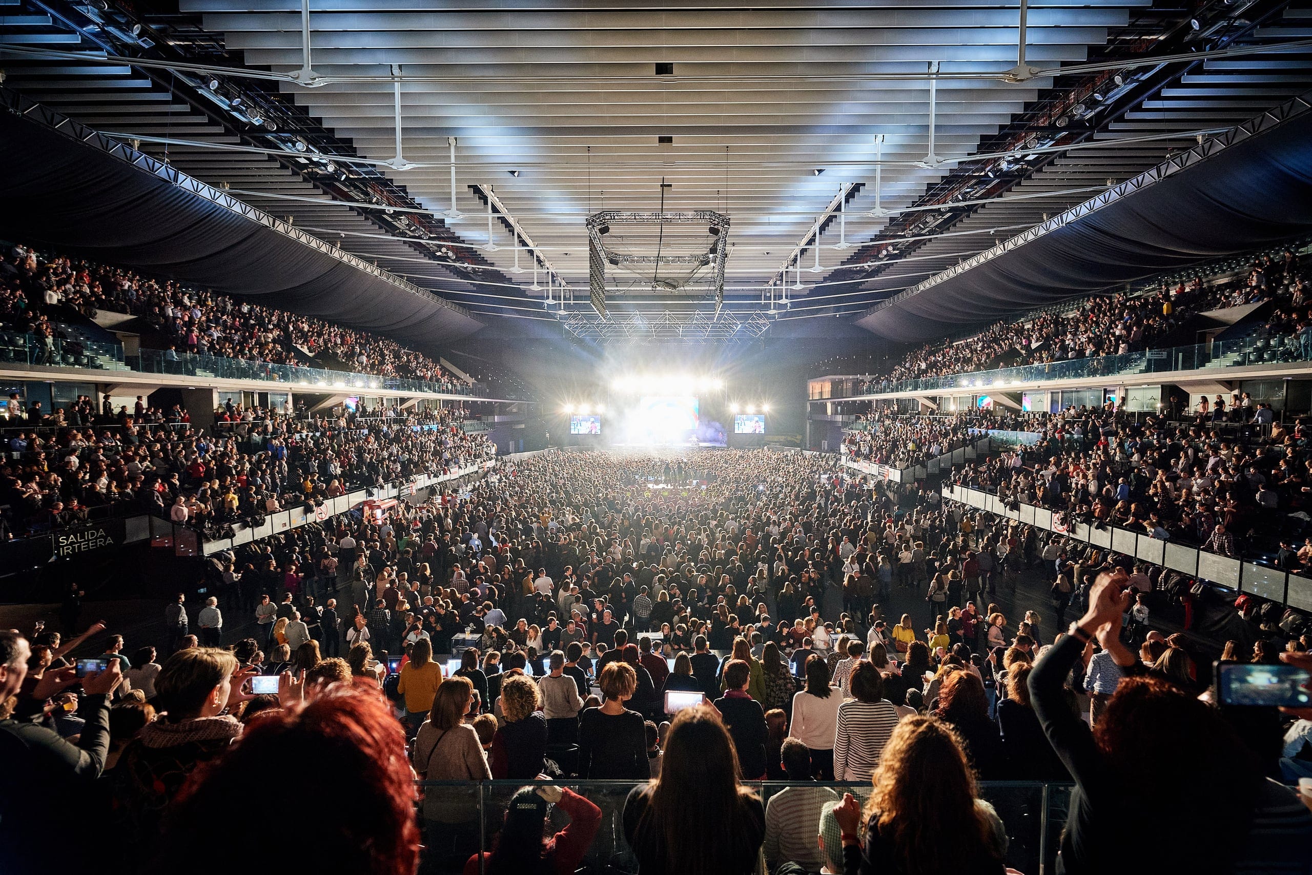 Arena llena vista desde el fondo, con el escenario encendido